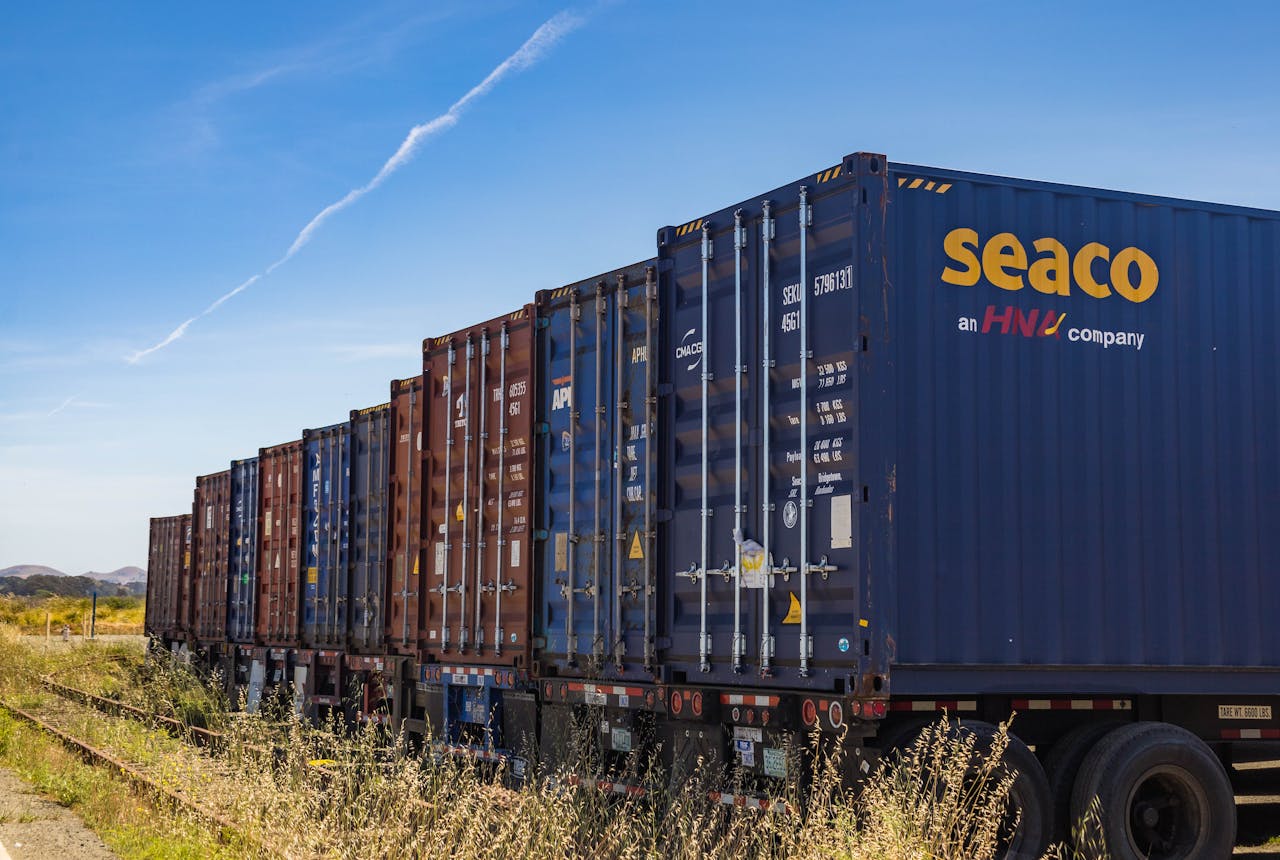 hero-img-01 Row of vibrant cargo containers on train tracks under a clear blue sky.